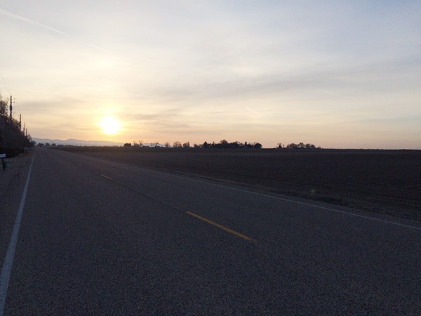 A wide open road with the sun setting in the background.