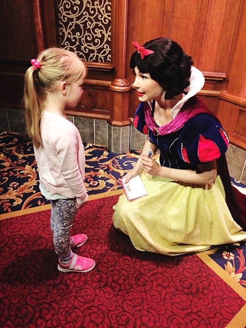 A little girl standing by a Disney princess.