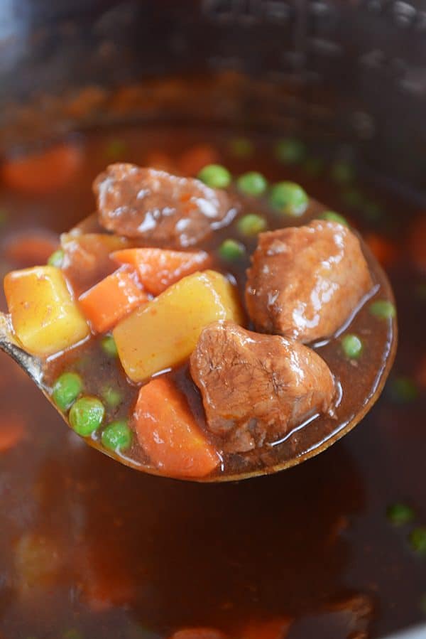 A ladle full of beef, potatoes, carrots, peas, and stew broth.