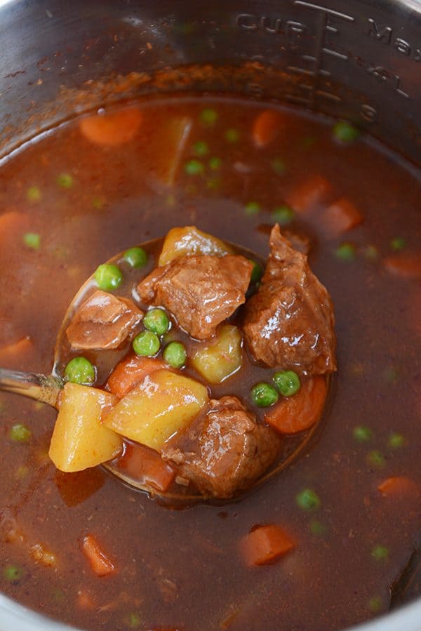 An Instant Pot bowl full of stew, with a ladle pulling a scoop of beef, potatoes, carrots, peas, and stew broth out. 