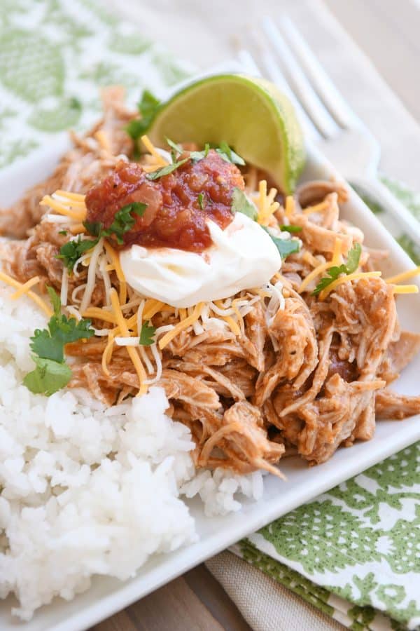 Instant pot Mexican pork on white tray with rice and beans and sour cream, salsa, and fresh limes.