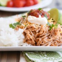 Instant pot Mexican pork on white tray with rice and beans and sour cream, salsa, and fresh limes.
