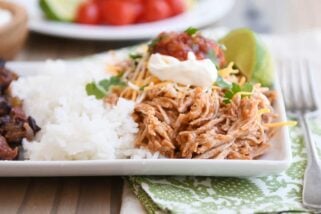 Instant pot Mexican pork on white tray with rice and beans and sour cream, salsa, and fresh limes.