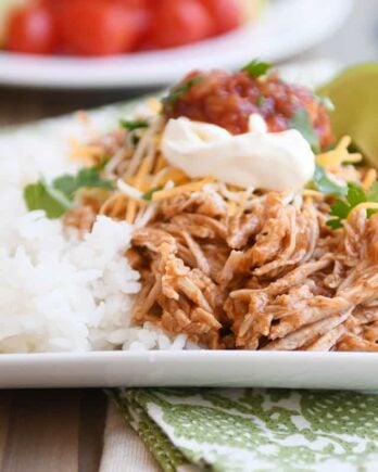 Instant pot Mexican pork on white tray with rice and beans and sour cream, salsa, and fresh limes.