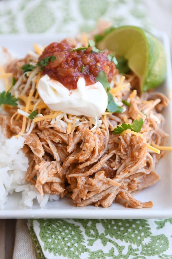 Instant pot Mexican pork on white tray with rice and beans and sour cream, salsa, and fresh limes.