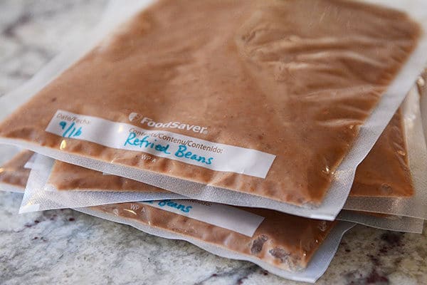 Four pouches of vacuum-sealed pouches of refried beans stacked on top of each other. 