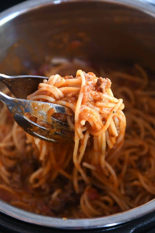 Instant pot spaghetti being lifted out of Instant Pot with tongs.