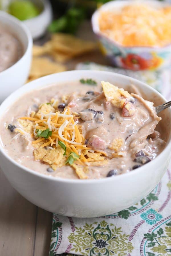Instant Pot white chicken chili in white bowl with spoon and shredded cheese.