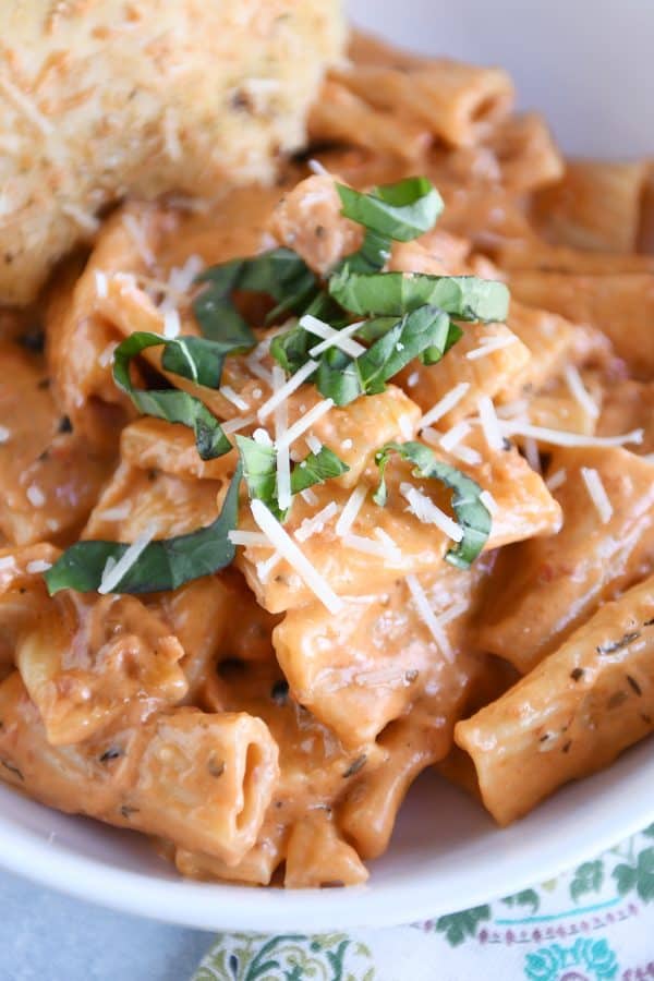 Close up of creamy baked ziti in white bowl with basil and parmesan.