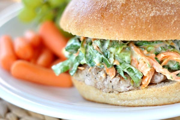 Turkey burger with romaine and carrot slaw on a white plate next to petite carrots.