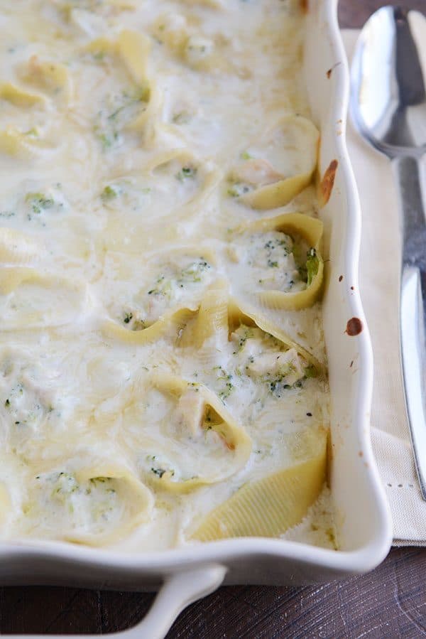 A white casserole dish filled with creamy stuffed broccoli alfredo pasta shells.
