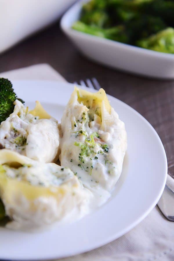 Three broccoli and alfredo-stuffed pasta shells on a white plate. 