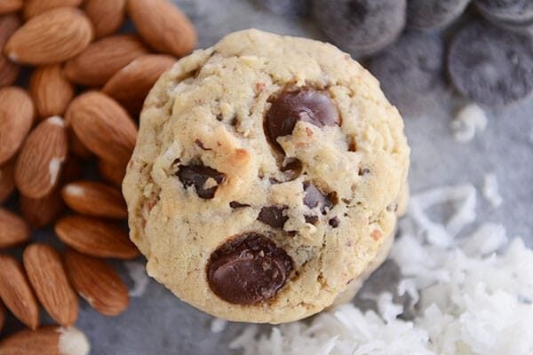 A chocolate chip cookie next to piles of almonds, chocolate chips, and shredded coconut.