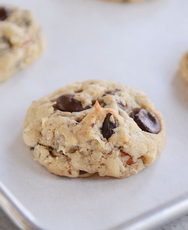 A cookie with large chocolate chunks and coconut on a cookie sheet.