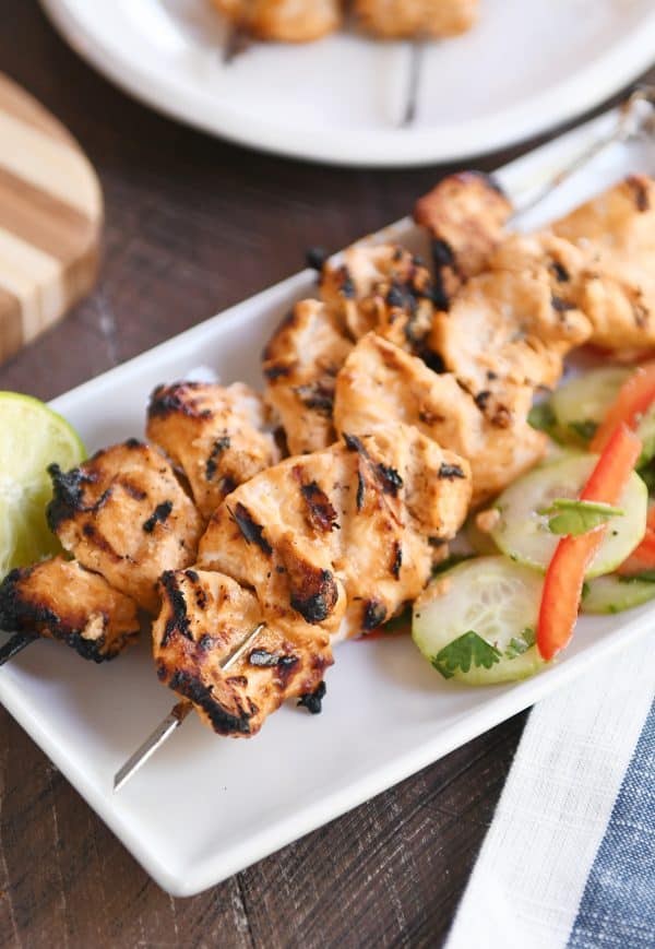 Cucumber salad with coconut milk chicken satay on white platter. 