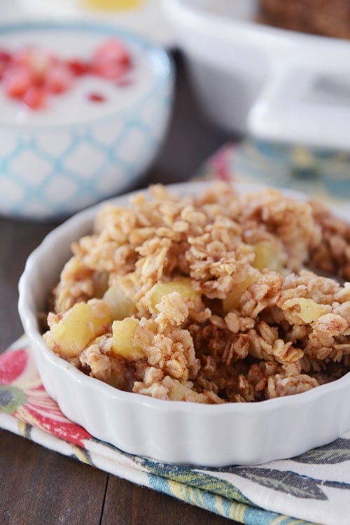 A small white bowl of baked oatmeal with chunks of cinnamon-coated apples. 