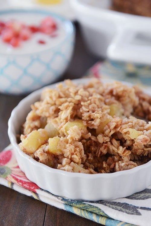 A small white bowl of baked oatmeal with chunks of cinnamon-coated apples.