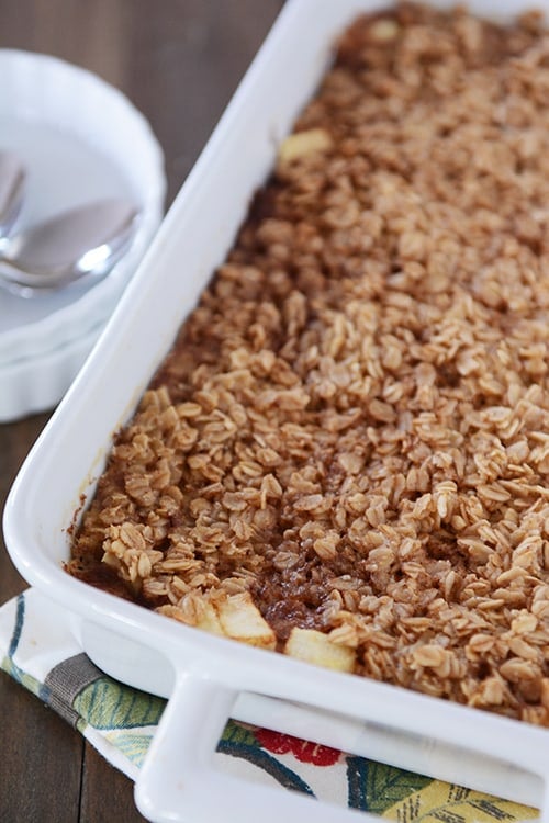 A white dish full of baked oatmeal with chunks of apple peeking out of the oatmeal at the front of the dish. 