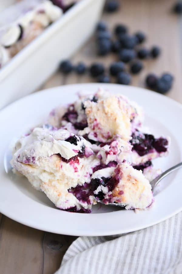 White dessert plate with scoop of heavenly blueberries and cream angel food cake dessert with bite on spoon.