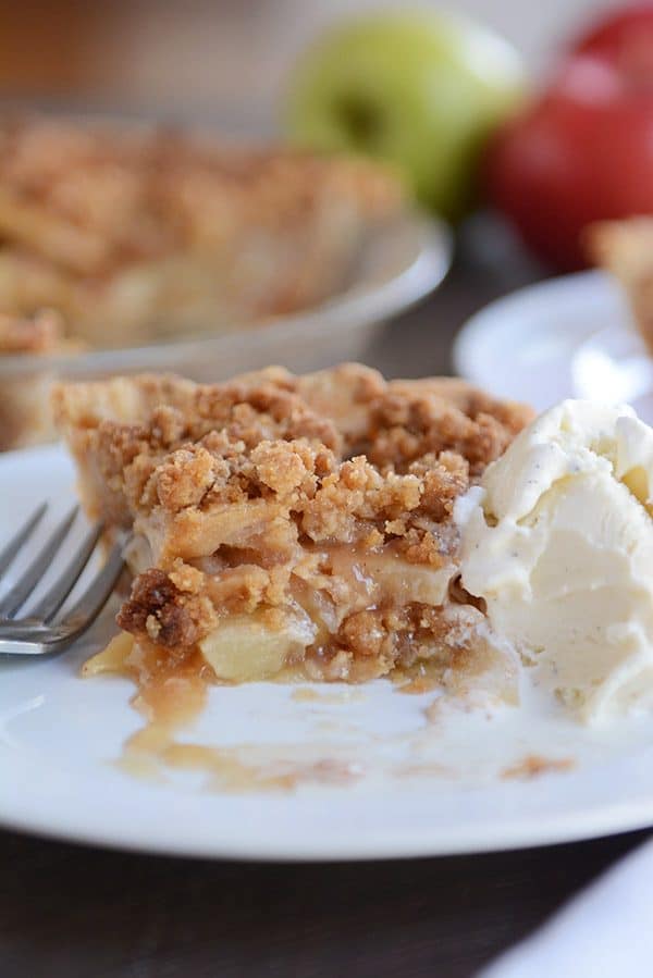 A slice of apple crumble pie with a bite taken out next to a scoop of ice cream.