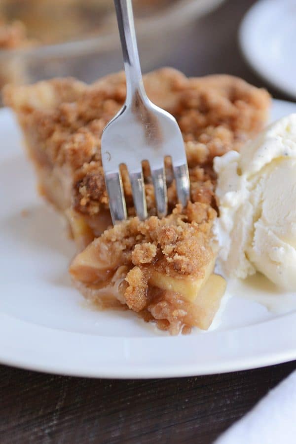 A fork taking a bite of apple crumble pie off of a slice.
