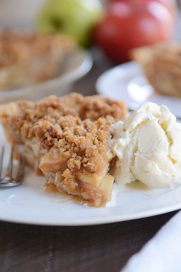 A slice of apple crumble pie and scoop of vanilla ice cream on a white plate.