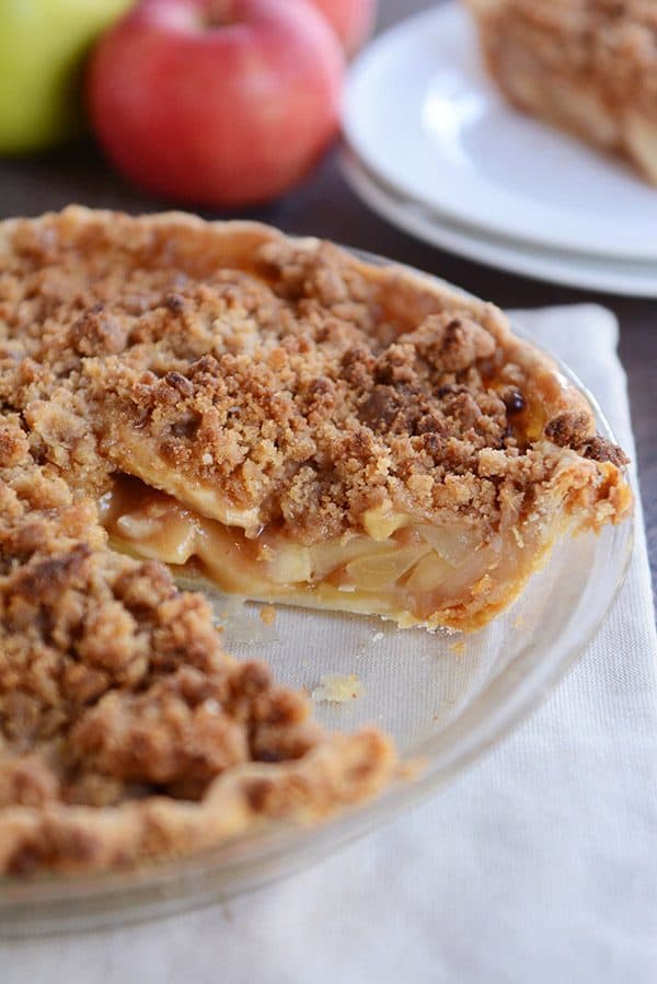 An apple crumble pie with a piece cut out in a glass pie dish.