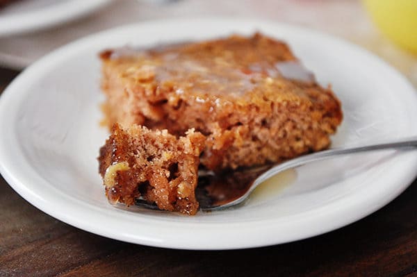 A piece of apple cake with sauce on top with a fork taking a bite out.