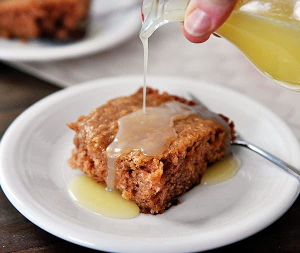 A piece of apple cake with a clear colored sauce being poured over the top.