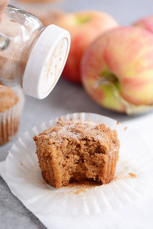 A muffin with a bite taken out getting cinnamon and sugar dusted on top. 