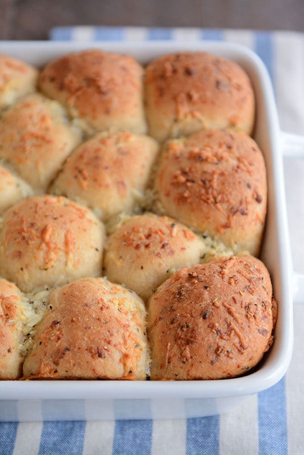 A white pan of golden brown cooked asiago topped rolls.