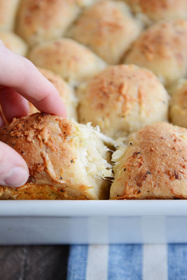 An Asiago roll getting pulled out of a pan of rolls. 