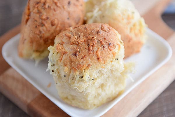 Three asiago cheese topped rolls on a small square plate.