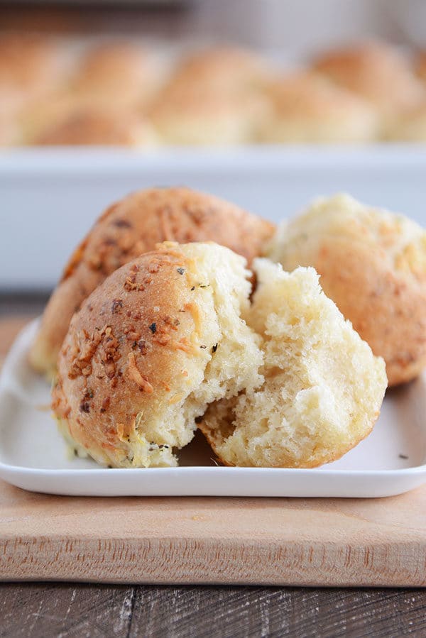 Asiago rolls on a white plate with the front roll split in half. 