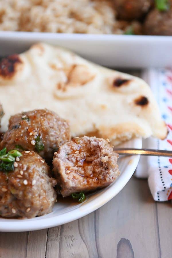 Bite taken out of Asian meatball with chili sauce on white plate with naan.