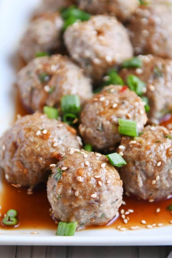 Asian meatballs drizzled in sauce on a white platter.