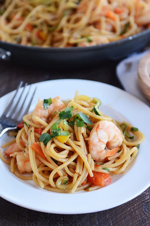 A white plate full of spaghetti noodles with vegetables and shrimp.