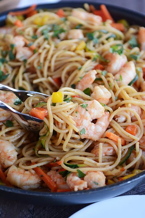 A skillet full of spaghetti noodles, shrimp, and chopped vegetables.