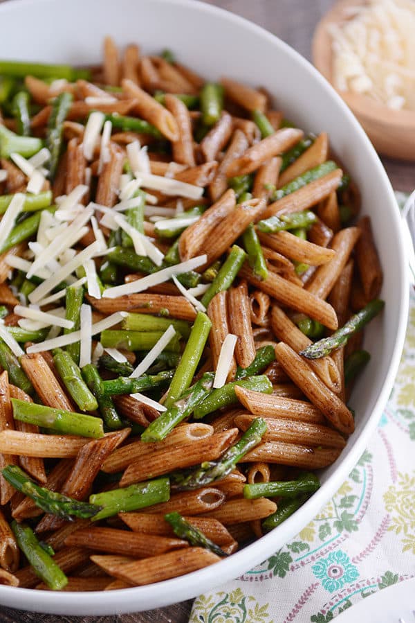 Top view of a large white oval bowl full of cooked penne and asparagus pieces.