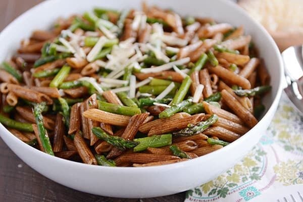 A large white bowl of balsamic coated penne pasta and asparagus pieces with shredded parmesan on top.