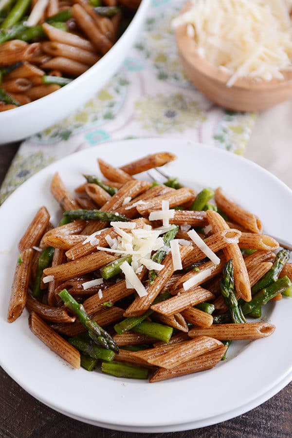 A white plate with cooked penne and asparagus and a sprinkle of parmesan cheese on top.