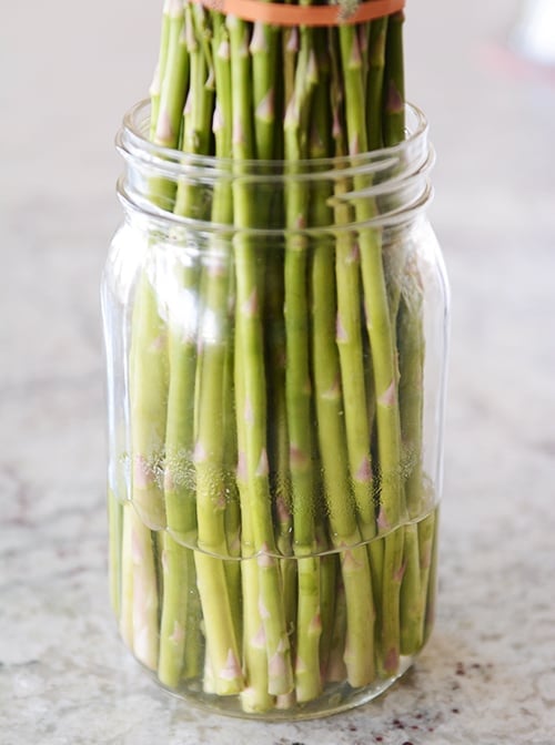 A mason jar with a rubber-banded bunch of asparagus and a few inches of water on the bottom.