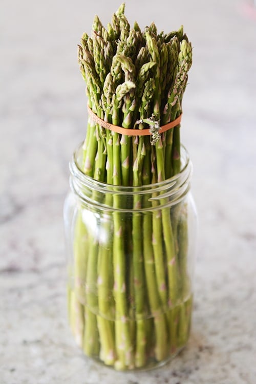 A mason jar with a bunch of asparagus and a few inches of water.