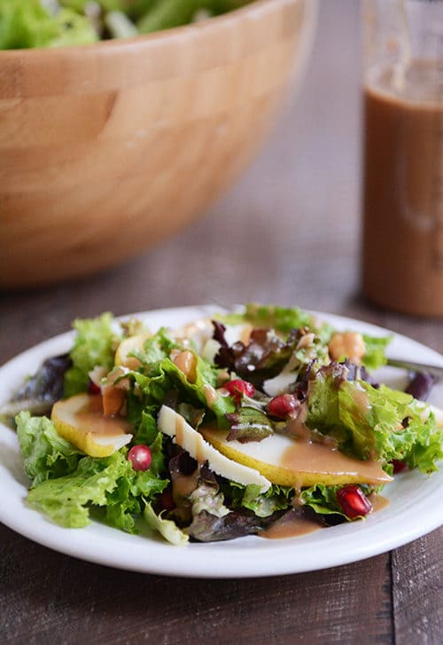 A green Autumn salad topped with dressing and fruit on a white plate.