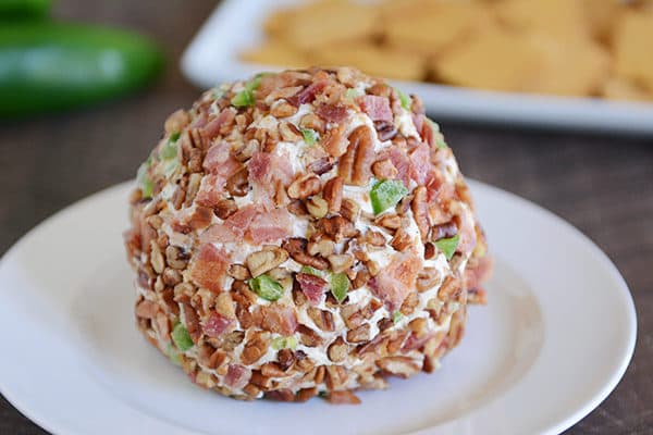 A bacon, jalapeno, and nut covered cheeseball on a white plate.