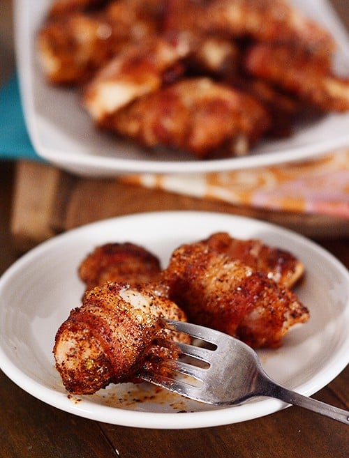 A fork picking up a bacon-wrapped chicken bite off of a plate of bites.