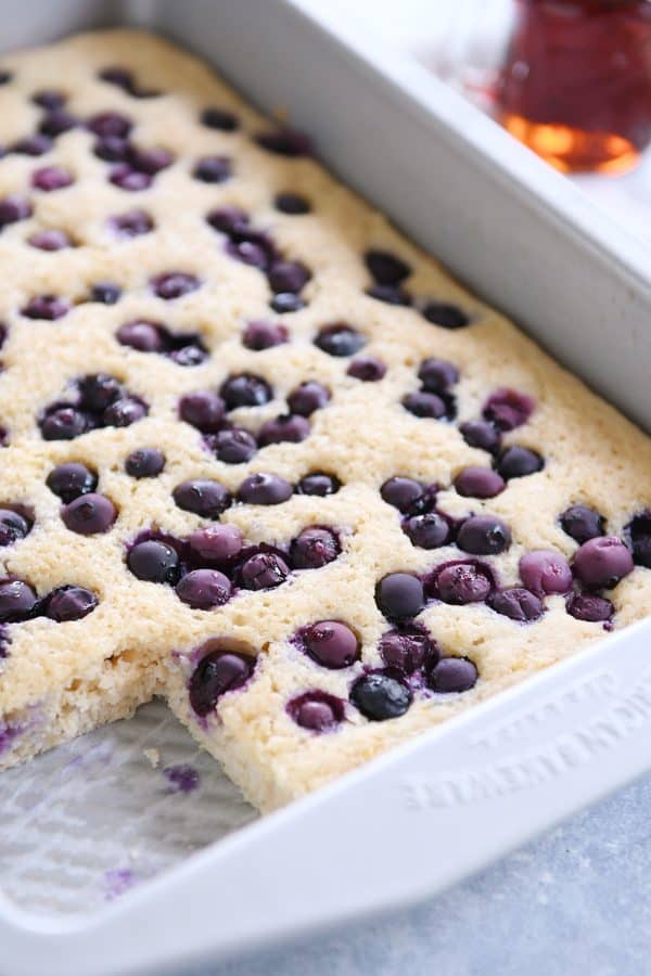 Baked pan of fluffy baked pancakes with blueberries on top with corner piece taken out.