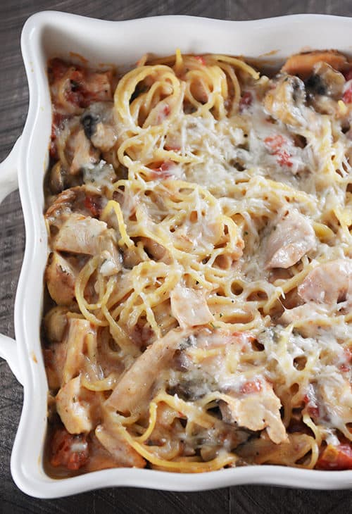 Top view of a white casserole dish full of cheesy spaghetti with chicken and mushrooms.