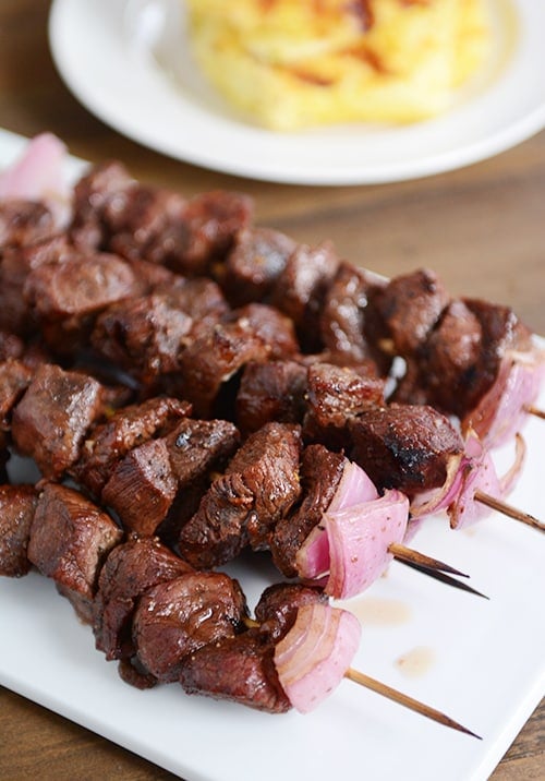 A white tray of beef and onion kebabs. 