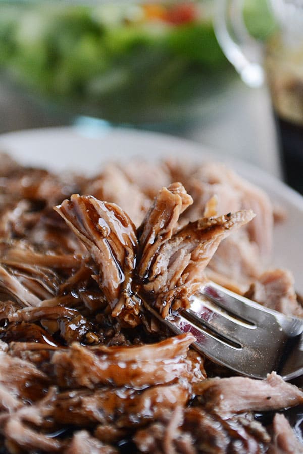 A forkful of shredded glazed pork over a full plate of pork, and a salad in the background. 